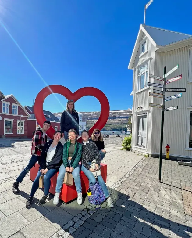 A group of students sit under a heart-shaped sculpture in the middle of a Akureyri street